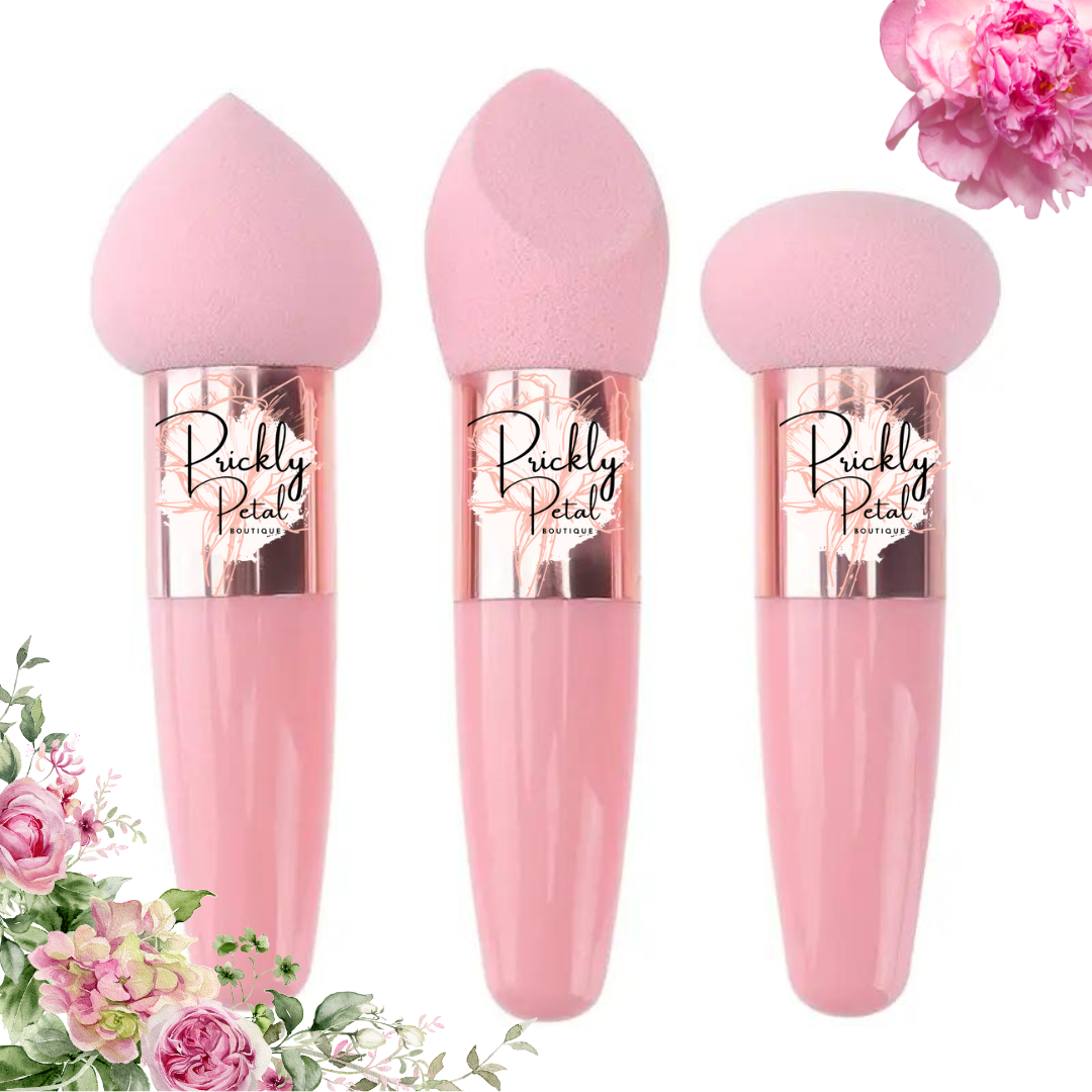 Three pink makeup sponges with handles, each with the Prickly Petal Boutique logo. The sponges are designed in different shapes, including a wedge and a handled blender, displayed against a floral background.
