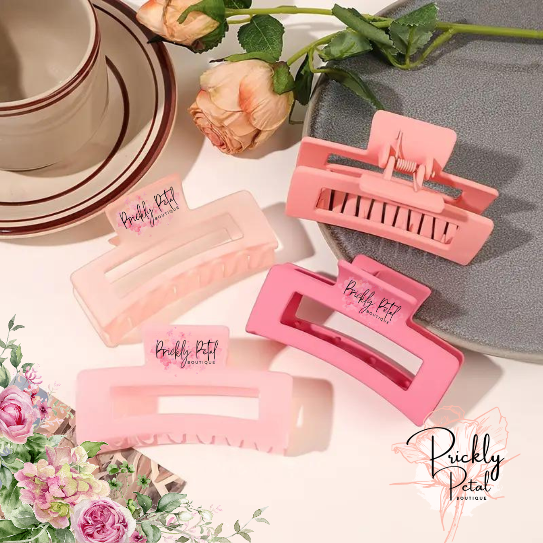 A set of pink rectangle claw hair clips from Prickly Petal Boutique, displayed on a table with floral decorations.