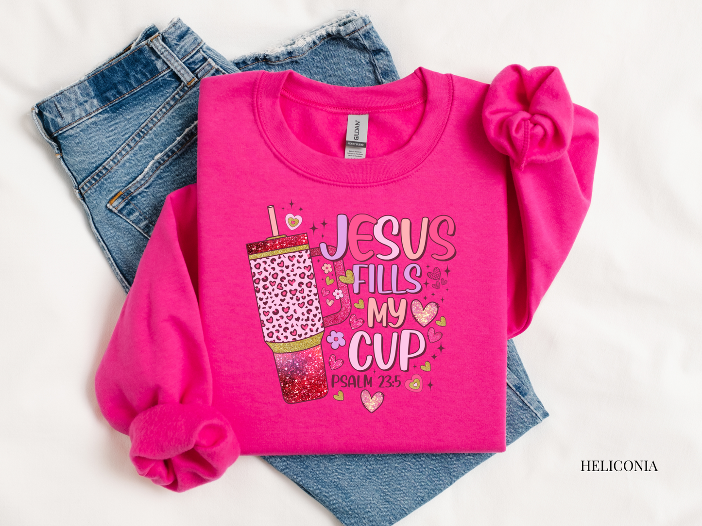 Pink sweatshirt with 'Jesus Fills My Cup' text and denim jeans on a white background