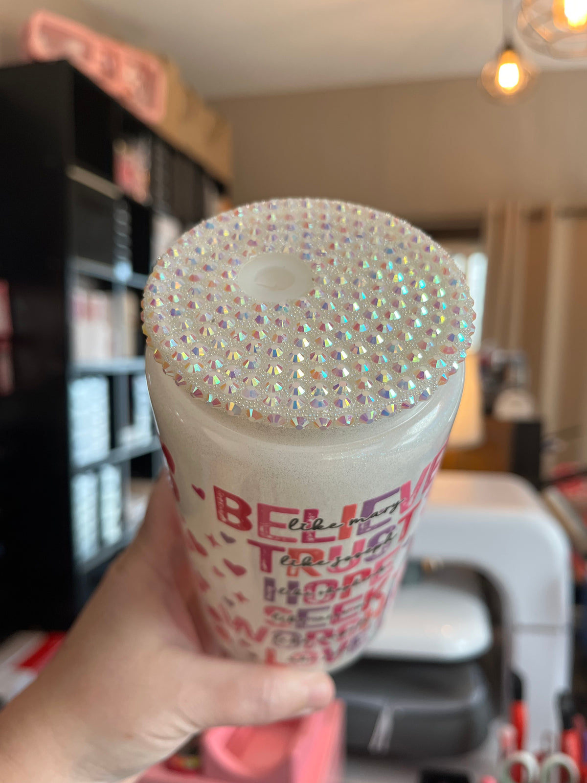 Hand holding a cup with rhinestone embellishments and text.