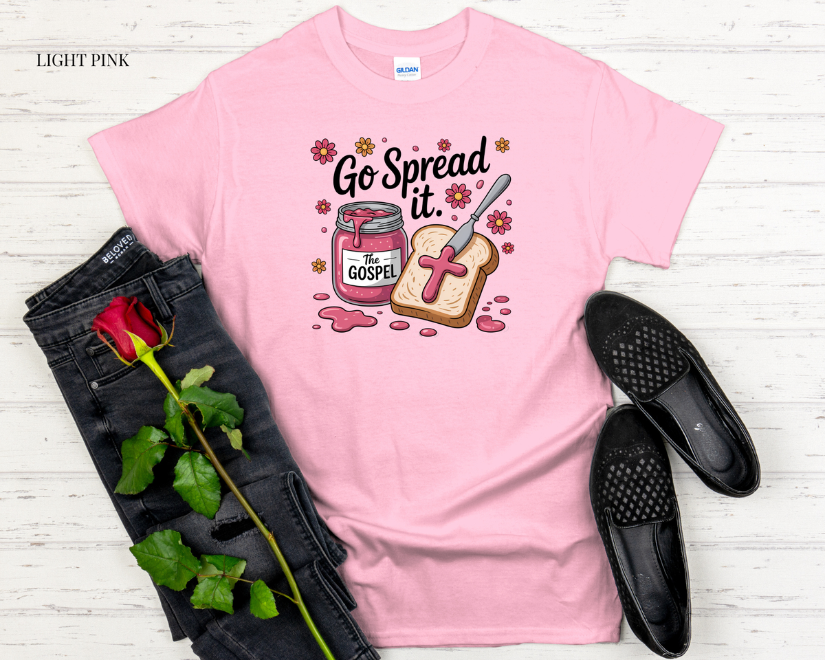 Pink t-shirt with graphic design featuring a jar of jelly and toast, accompanied by black jeans and black shoes on a light wooden surface.