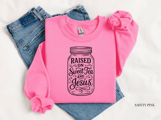 Pink sweatshirt with 'Raised on Sweet Tea and Jesus' design on blue jeans