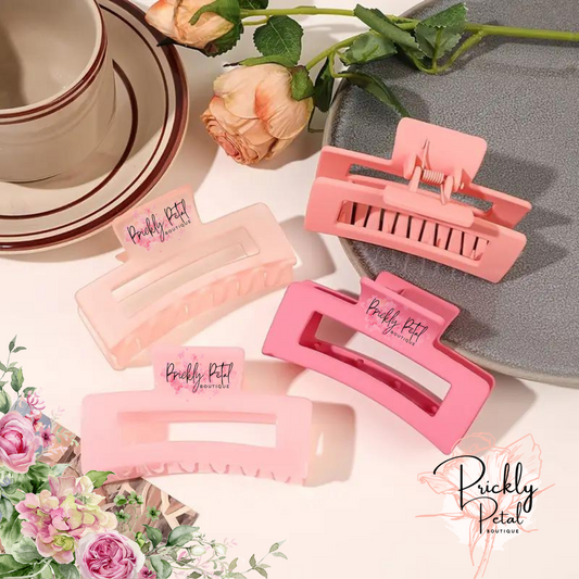 A set of pink rectangle claw hair clips from Prickly Petal Boutique, displayed on a table with floral decorations.