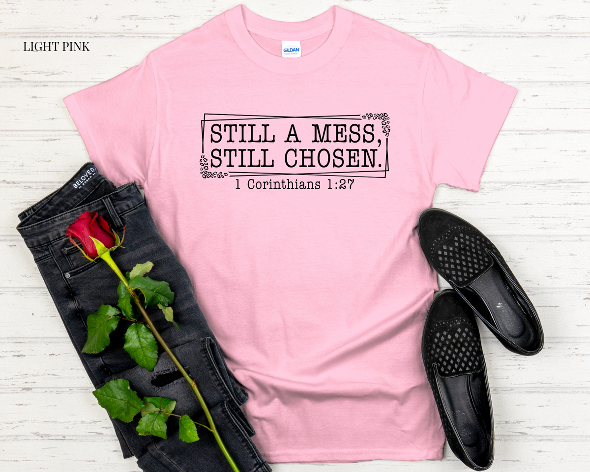 Light pink t-shirt with text, black jeans, black shoes, and a red rose on a light wooden surface.