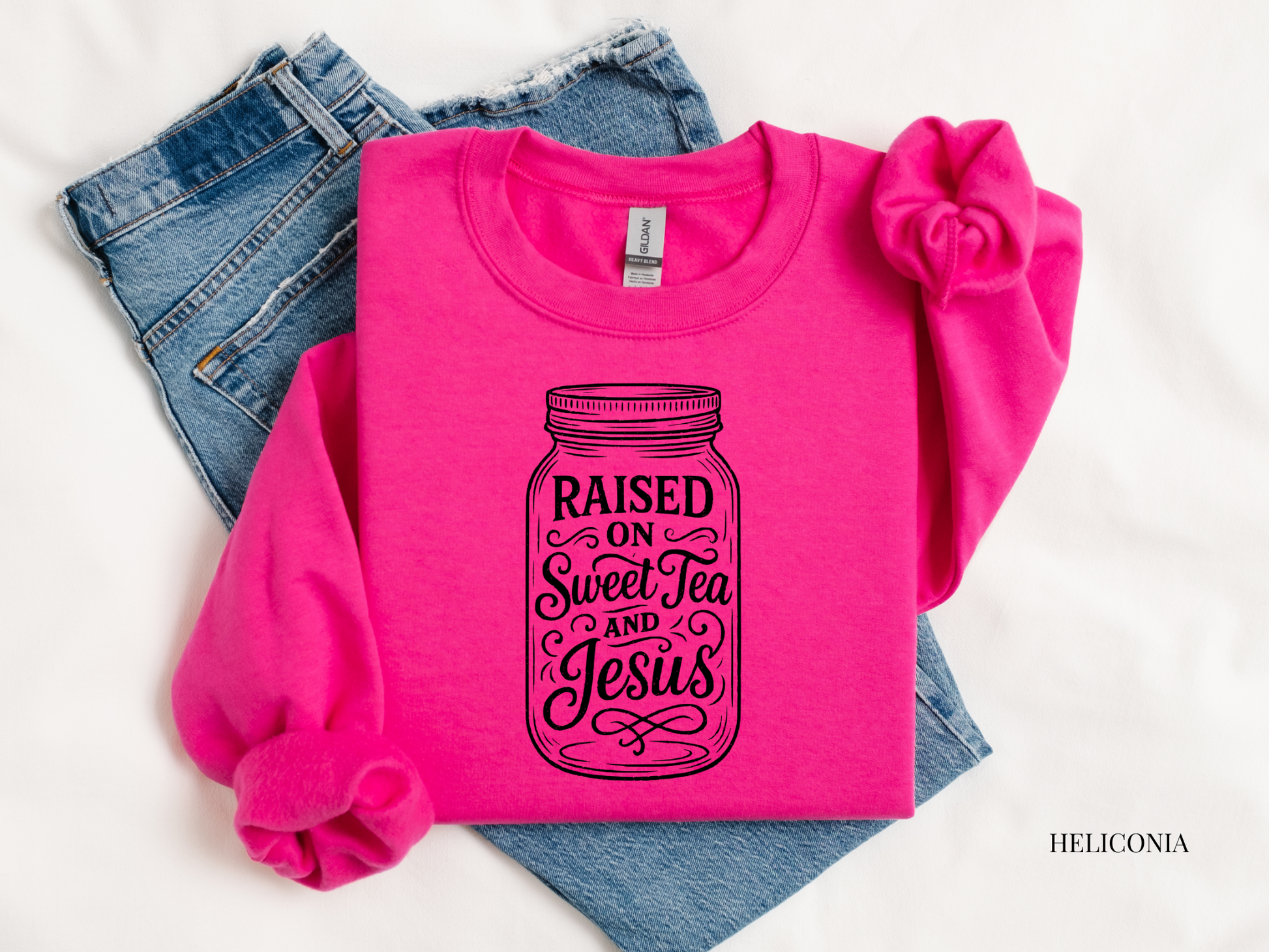 Pink sweatshirt with 'Raised on Sweet Tea and Jesus' text, paired with jeans and a headband on a white background.