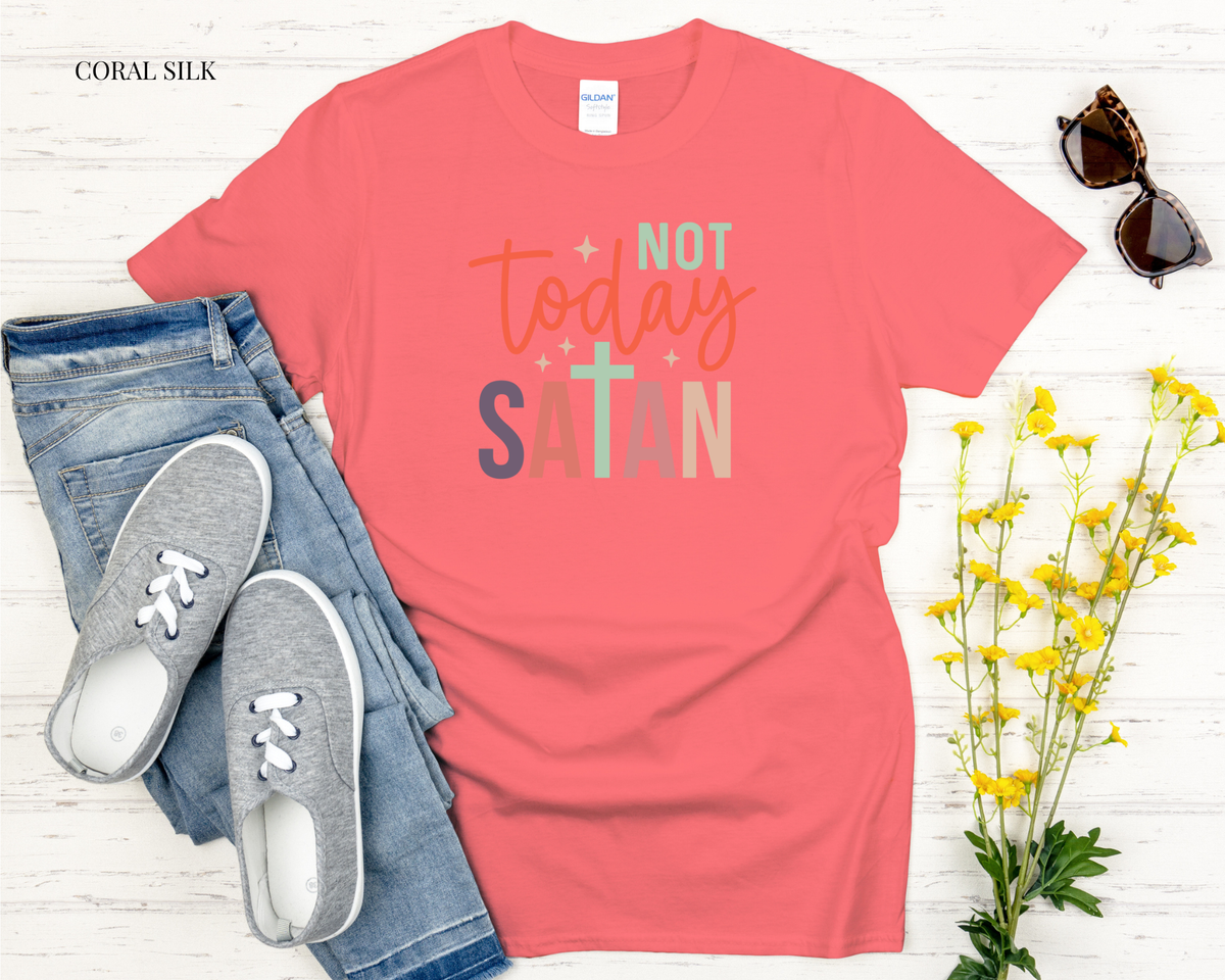 Coral t-shirt with 'Not Today Satan' text, jeans, sneakers, and sunglasses on a light wooden surface.
