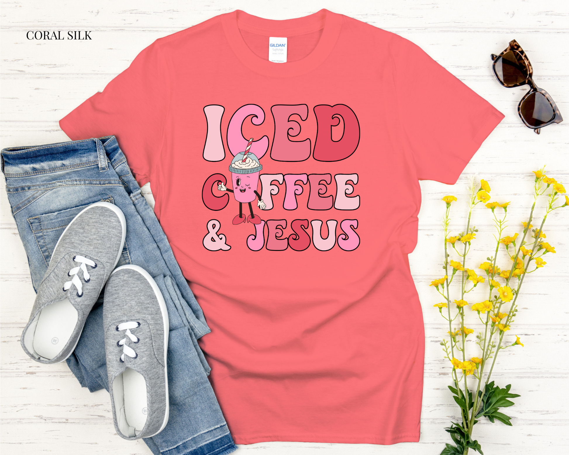 Coral t-shirt with 'ICED COFFEE & JESUS' text, jeans, sneakers, and sunglasses on a white background
