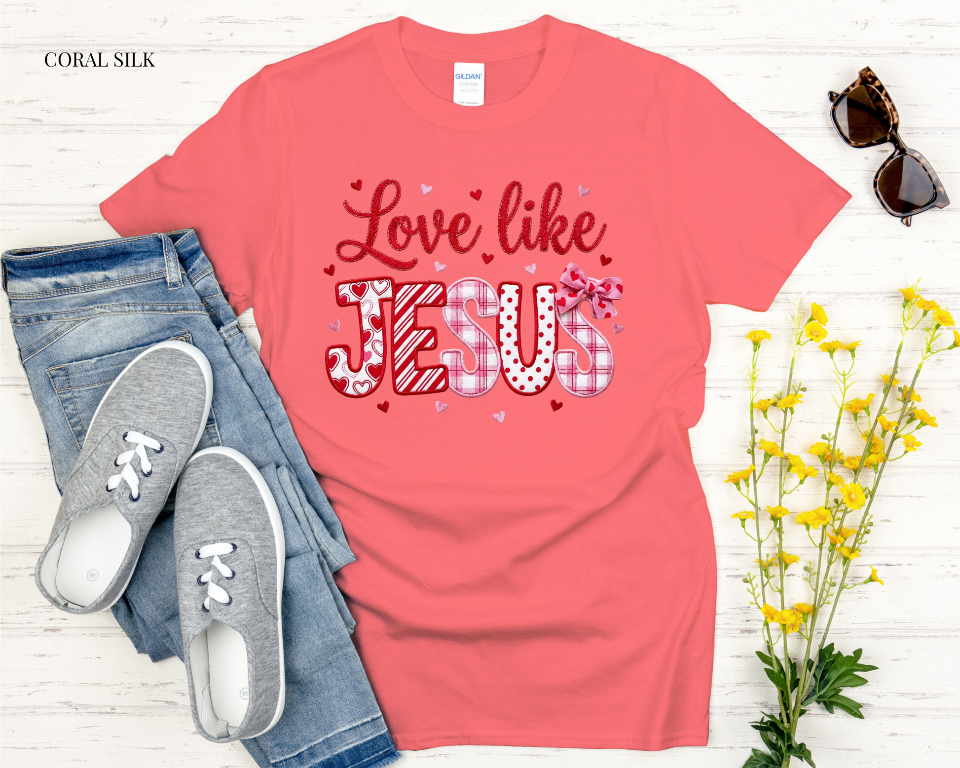 Coral t-shirt with 'Love like Jesus' text, paired with jeans and sneakers on a light wooden surface.