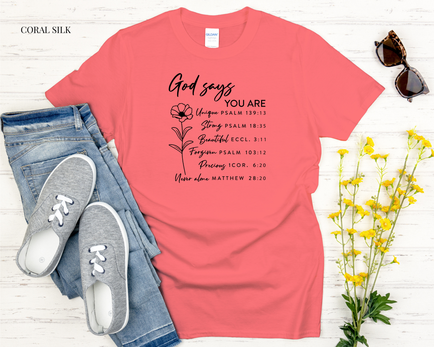 Coral t-shirt with motivational text, jeans, sneakers, sunglasses, and flowers on a white background