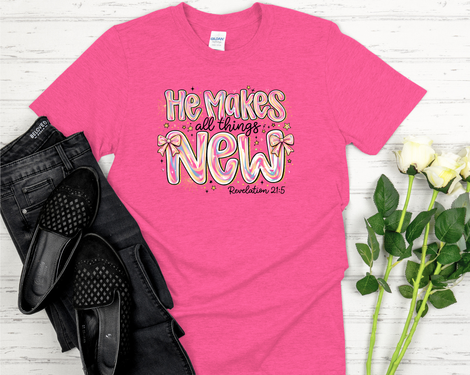 Pink t-shirt with design on a white wooden surface with black shoes and flowers.