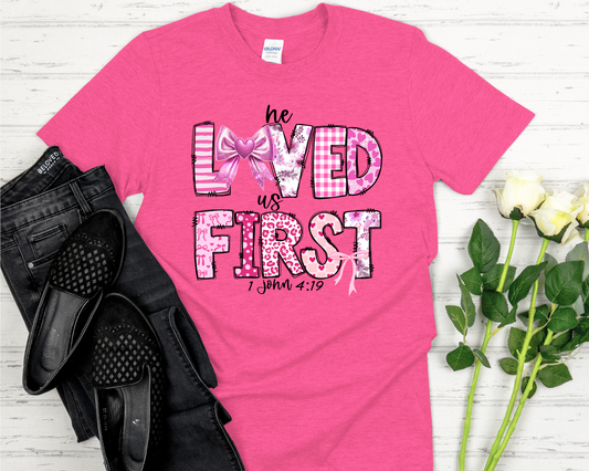 Pink t-shirt with design on a white wooden surface with black shoes and flowers.