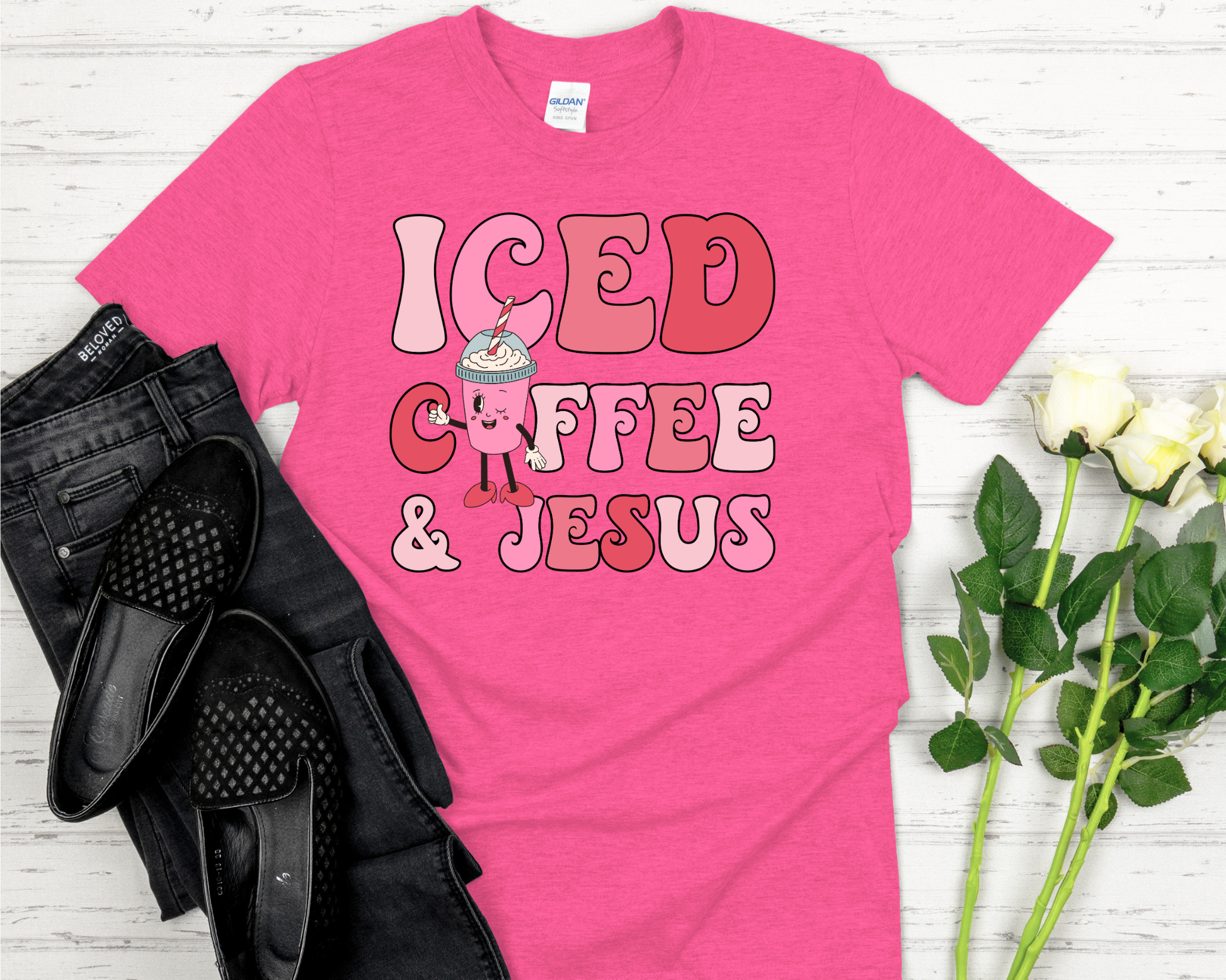 Pink t-shirt with design on a white wooden surface with black shoes and flowers.
