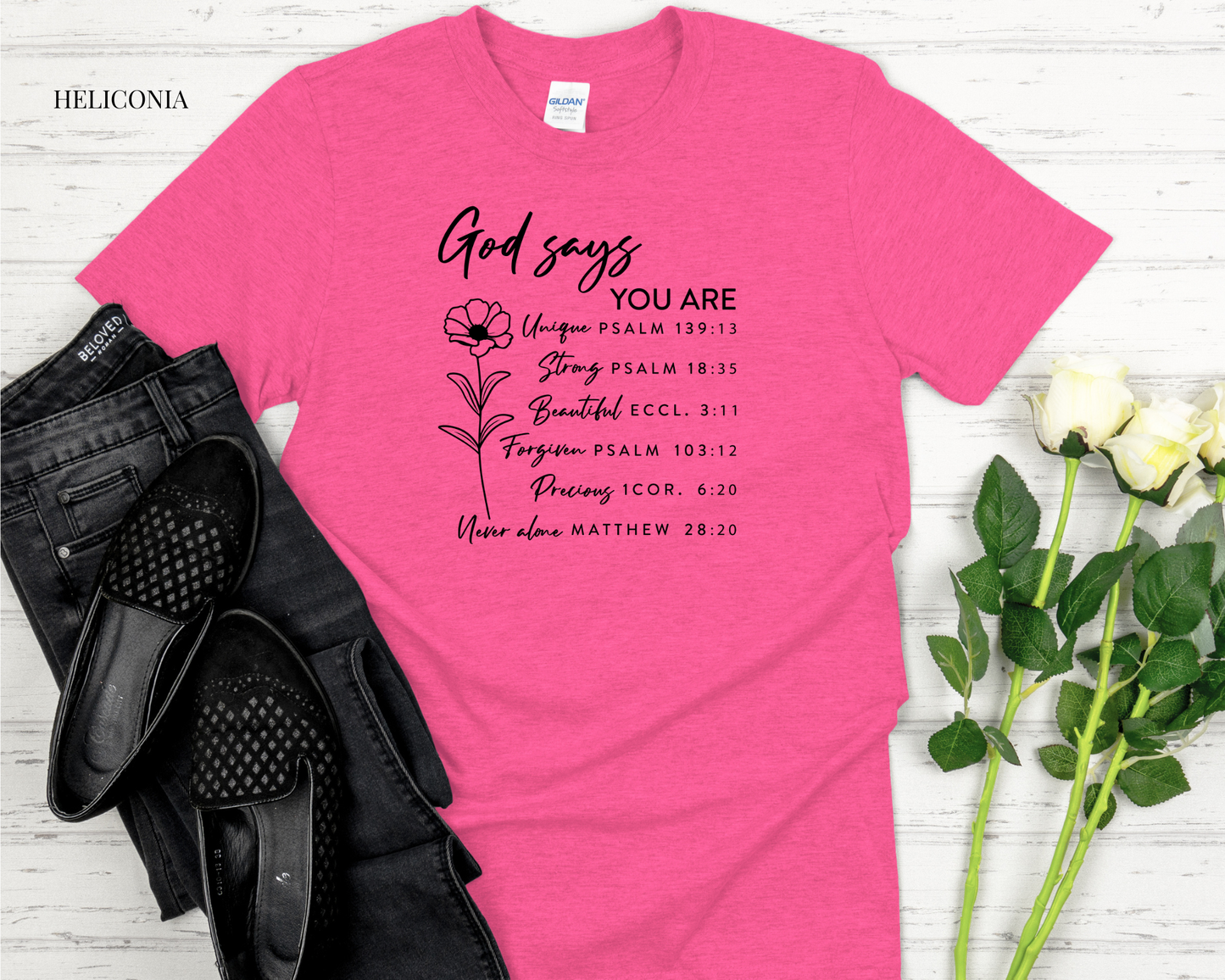 Pink t-shirt with motivational text on a white wooden surface with black shoes and flowers.