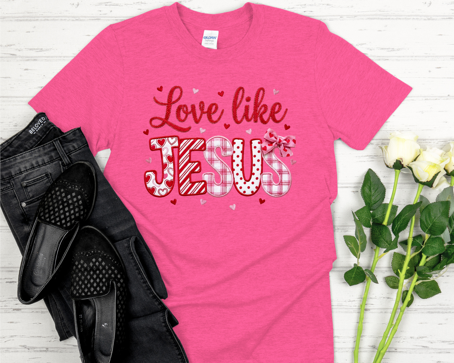 Pink t-shirt with design on a white wooden surface with black shoes and flowers.
