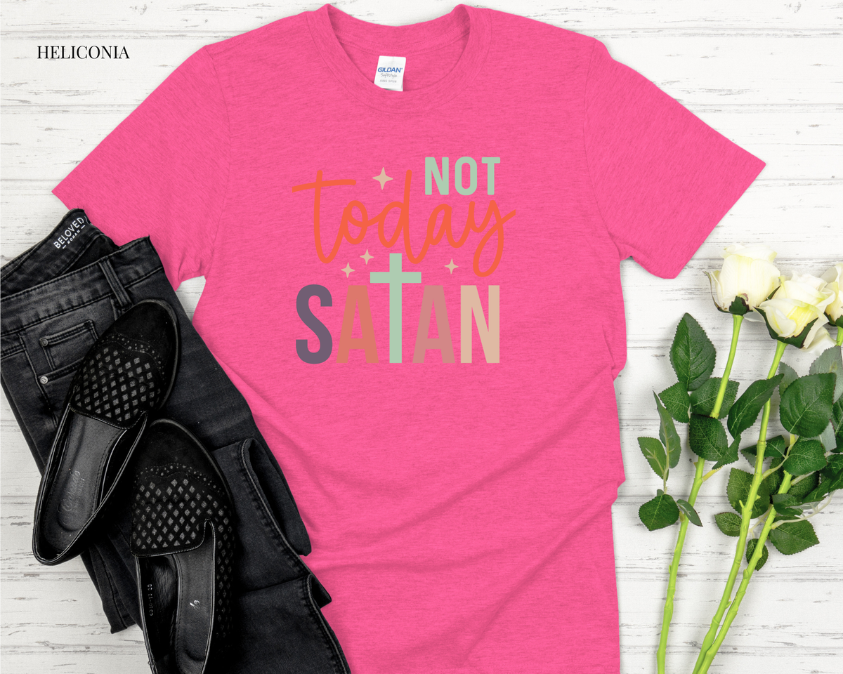 Pink t-shirt with 'Not Today Satan' text on a white wooden surface with black shoes and flowers.