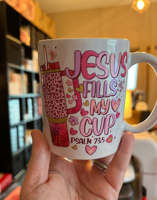 White mug with pink text and design held by a hand, blurred background