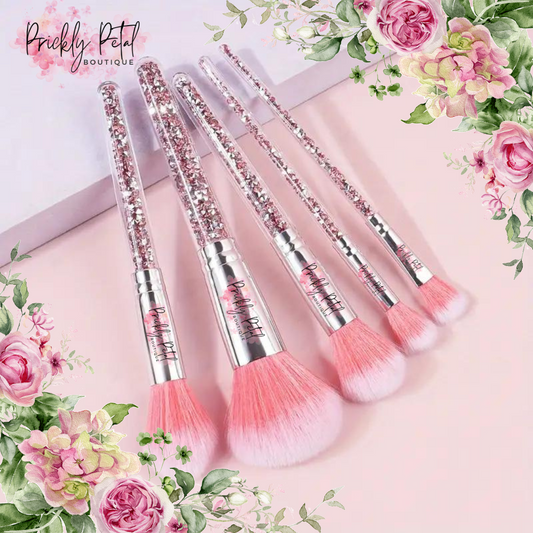 A set of makeup brushes with pink bristles and decorative elements on the handles, displayed on a surface with floral decorations.