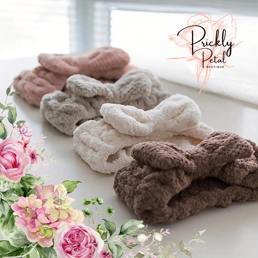A collection of fleece makeup headbands in beige, brown, and pink colors with a bowknot detail, displayed on a surface with floral decorations.