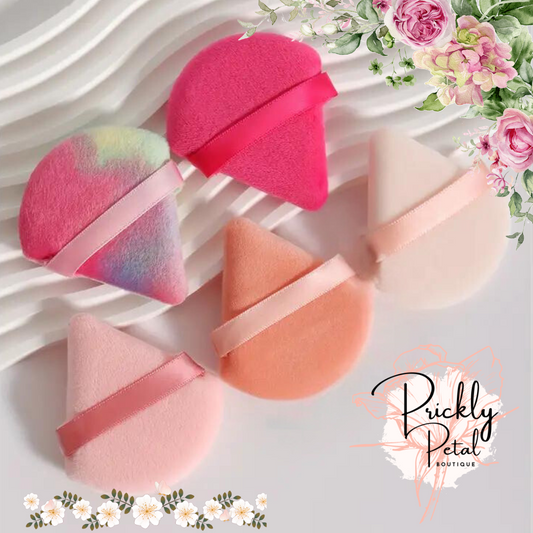 A set of triangular-shaped makeup sponges in various shades of pink and orange, displayed on a white surface with floral graphics in the corner.